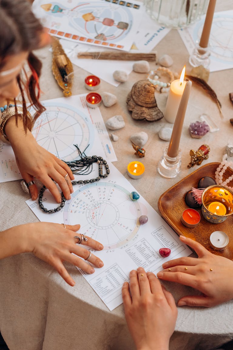 Hands arranging astrology charts, finding patterns guiding you with candles and crystals on a table for a spiritual ritual.